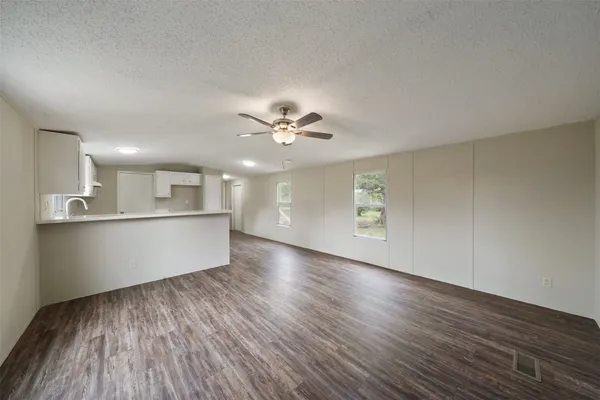 a view of an empty room with wooden floor and a kitchen