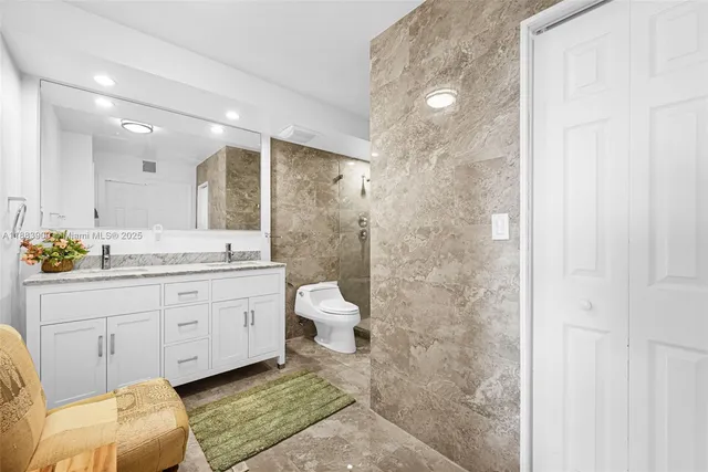 a bathroom with a granite countertop sink a toilet a mirror and shower