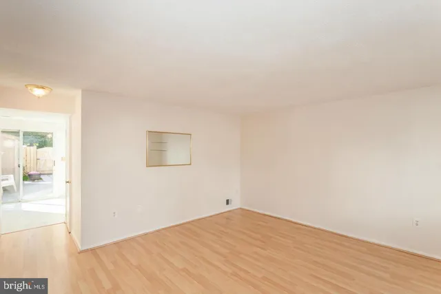 an empty room with wooden floor and a way to kitchen