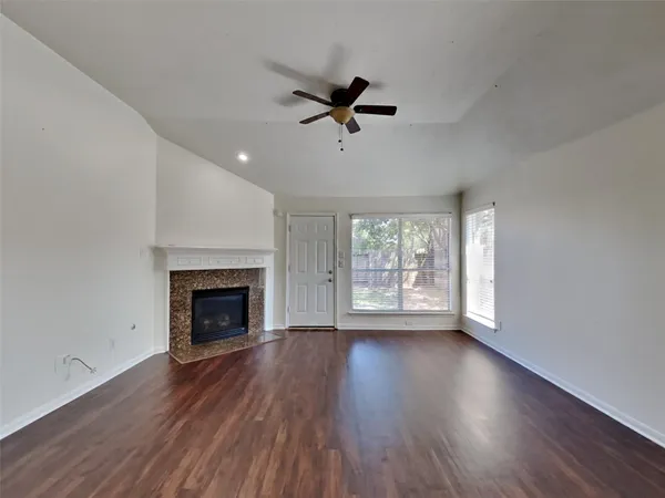 a view of an empty room with wooden floor fireplace and a window