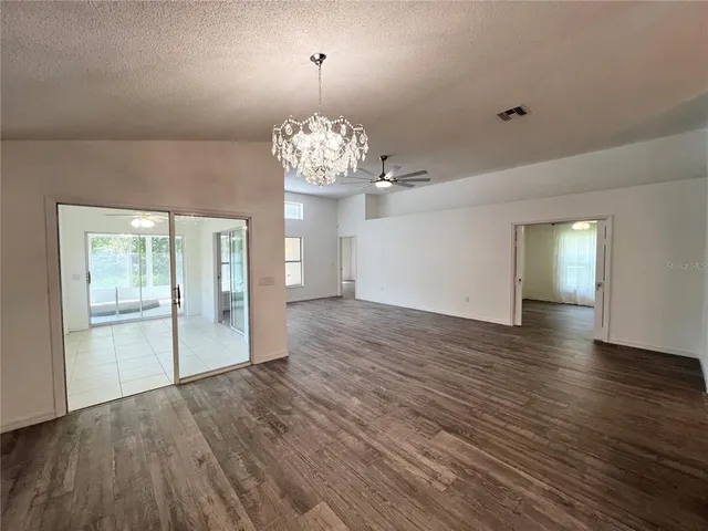 an empty room with wooden floor chandelier and windows