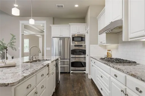a kitchen with stainless steel appliances granite countertop a dining table chairs refrigerator and microwave