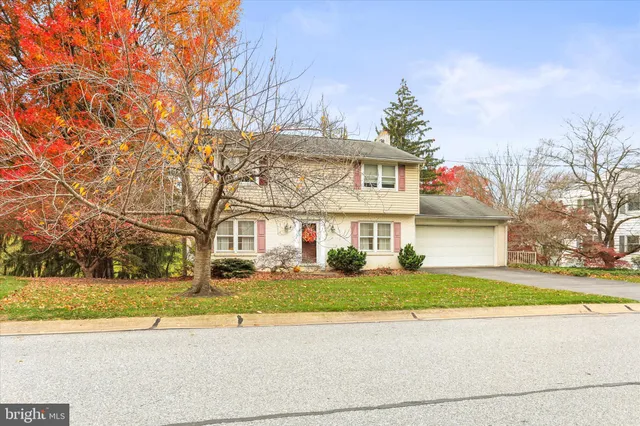 a view of a white house next to a yard with large trees