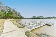 515 Mill Creek Road Pinehurst, TX 77362 - Photo 46 of 48 Serene lakeside setting with a dock and a paved walkway surrounded by greenery, ideal for outdoor relaxation and activities.