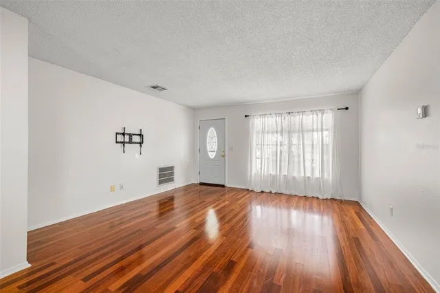 a view of an empty room with wooden floor and a window