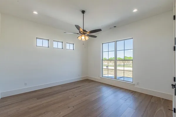 an empty room with wooden floor chandelier fan and windows