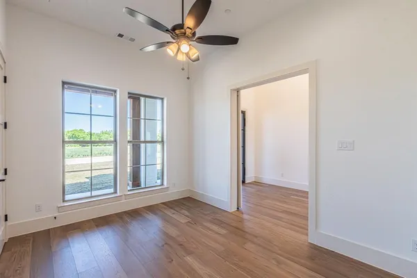 an empty room with wooden floor fan and windows