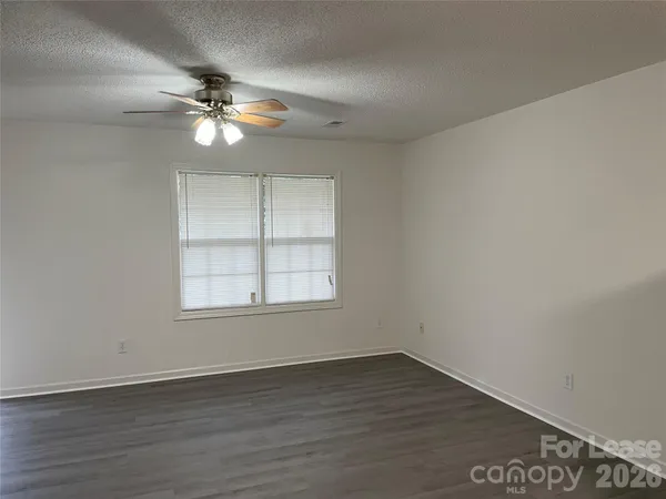 an empty room with wooden floor fan and windows