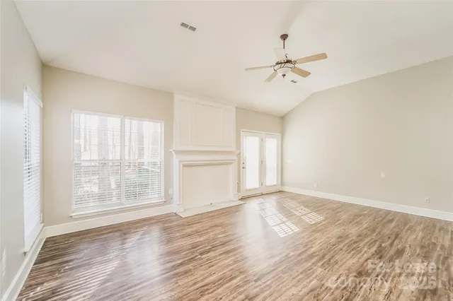 an empty room with wooden floor ceiling fan and windows