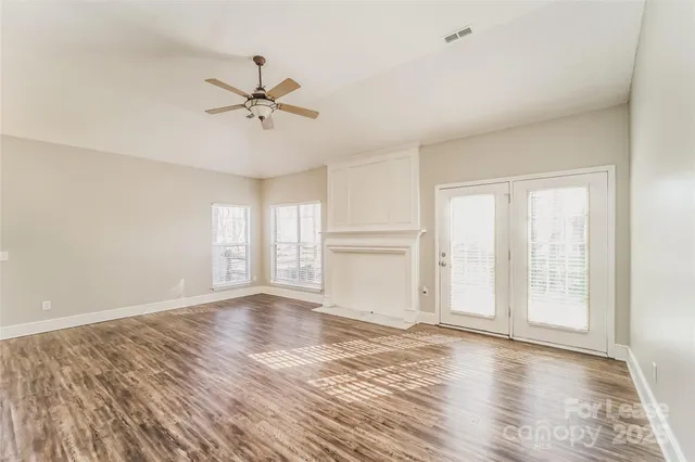an empty room with wooden floor fan and windows