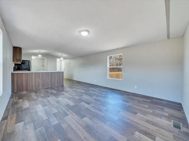 a view of an empty room with wooden floor and a kitchen