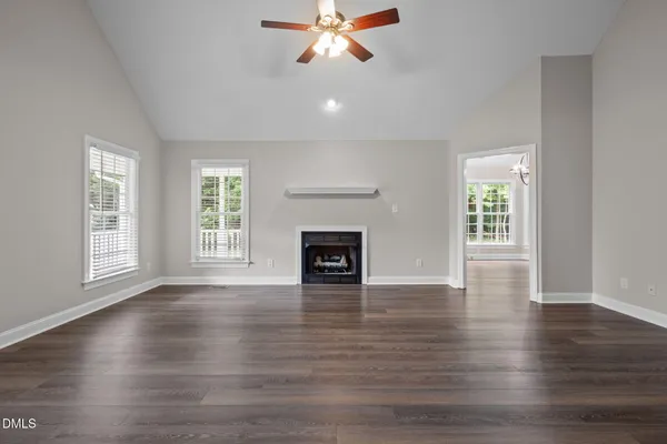 an empty room with wooden floor fireplace and windows