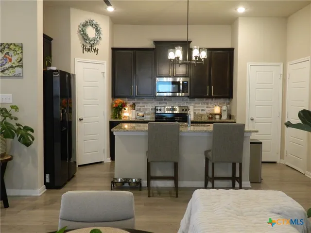 a kitchen with stainless steel appliances granite countertop a refrigerator a stove a sink a dining table and chairs with wooden floor