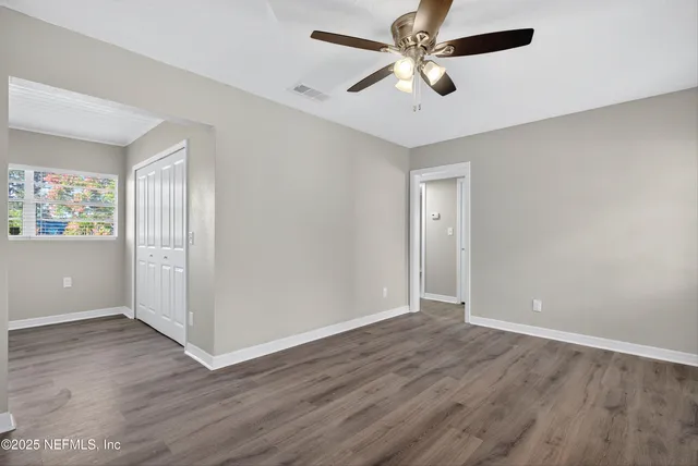 an empty room with wooden floor fan and windows