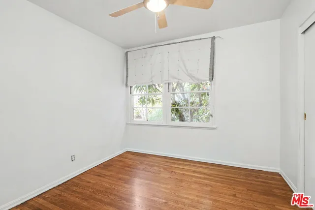 an empty room with wooden floor chandelier fan and windows
