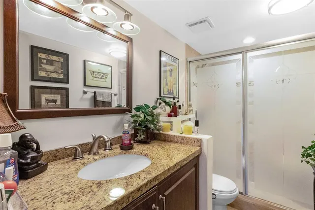 a bathroom with a granite countertop sink a toilet a mirror and shower