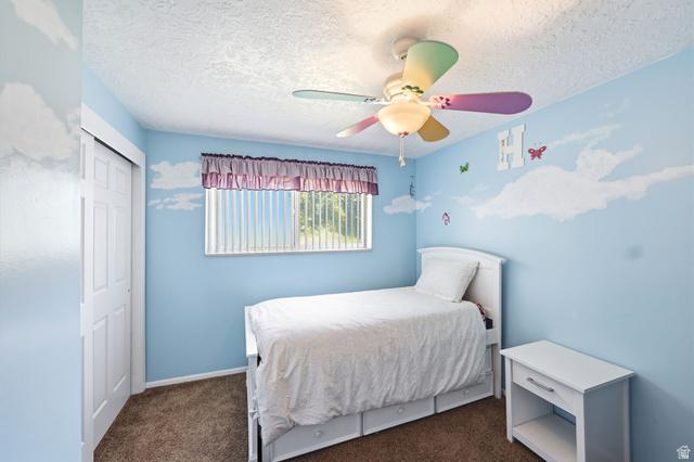 314 West Center Street, Unit F102 Bountiful, UT 84010 - Photo 19 of 29 Bedroom featuring blue walls with cloud detailing, a textured ceiling, a window with vertical blinds, and a ceiling fan with multi-colored blades