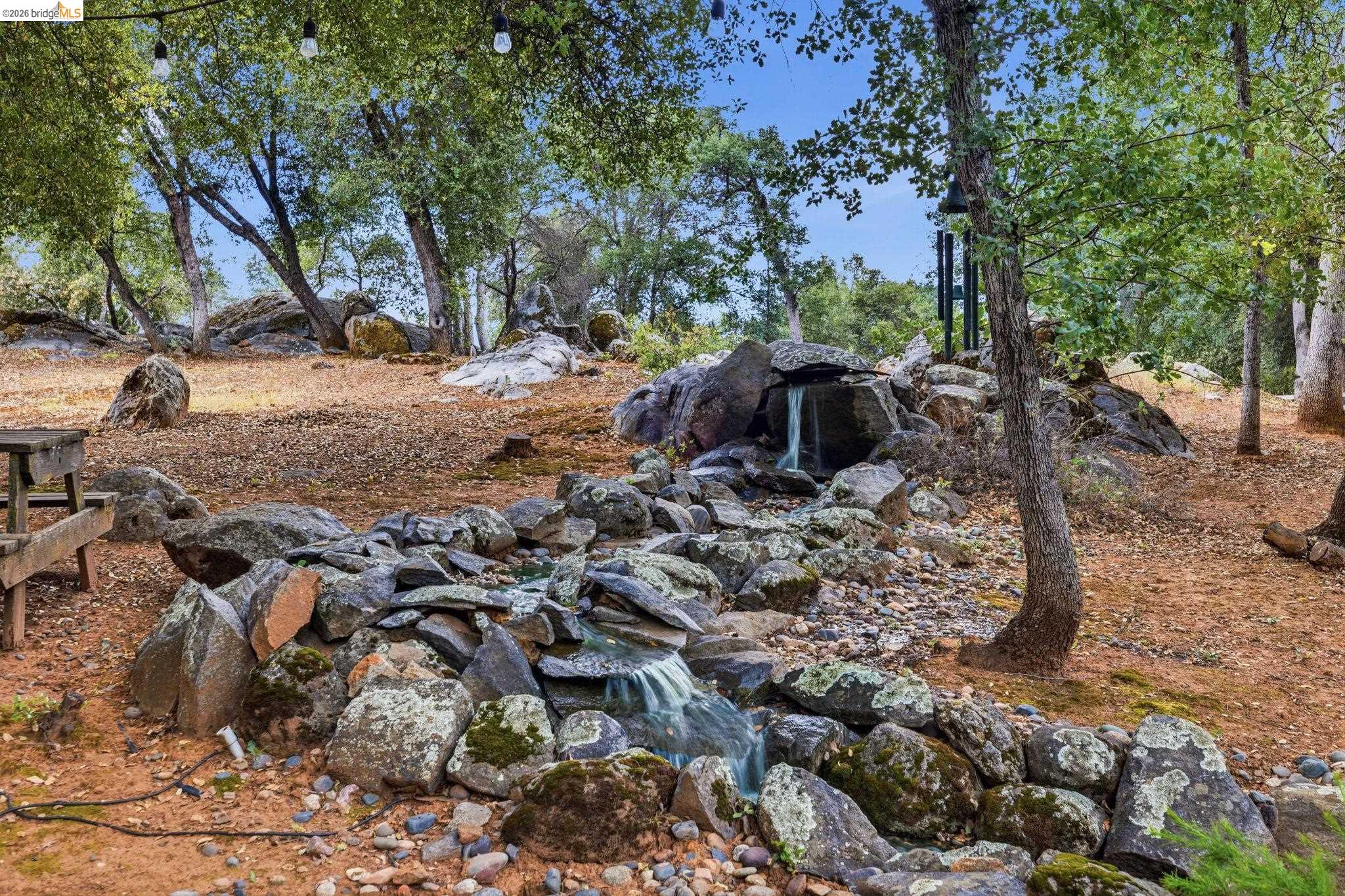 18450 Lambert Lake Road Sonora, CA 95370 - Photo 65 of 87 Natural rock water feature with a waterfall and winding stream, surrounded by mature trees and exposed boulders