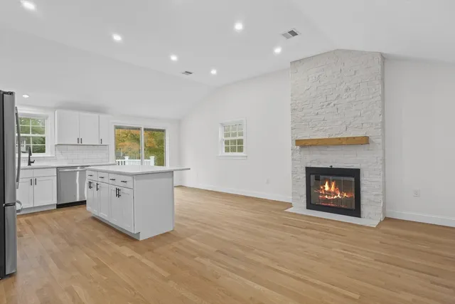 a kitchen with stainless steel appliances granite countertop a stove top oven a sink dishwasher and a fireplace with wooden floor