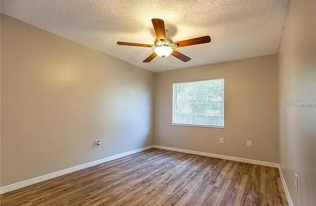 an empty room with wooden floor ceiling fan and windows