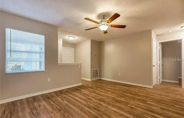 a view of empty room with wooden floor and fan