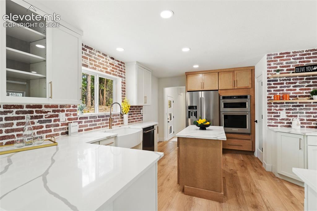 11665 Greentree Road Colorado Springs, CO 80908 - Photo 14 of 43 Kitchen with brick wall, light stone countertops, a center island, light wood-style floors, and stainless steel appliances
