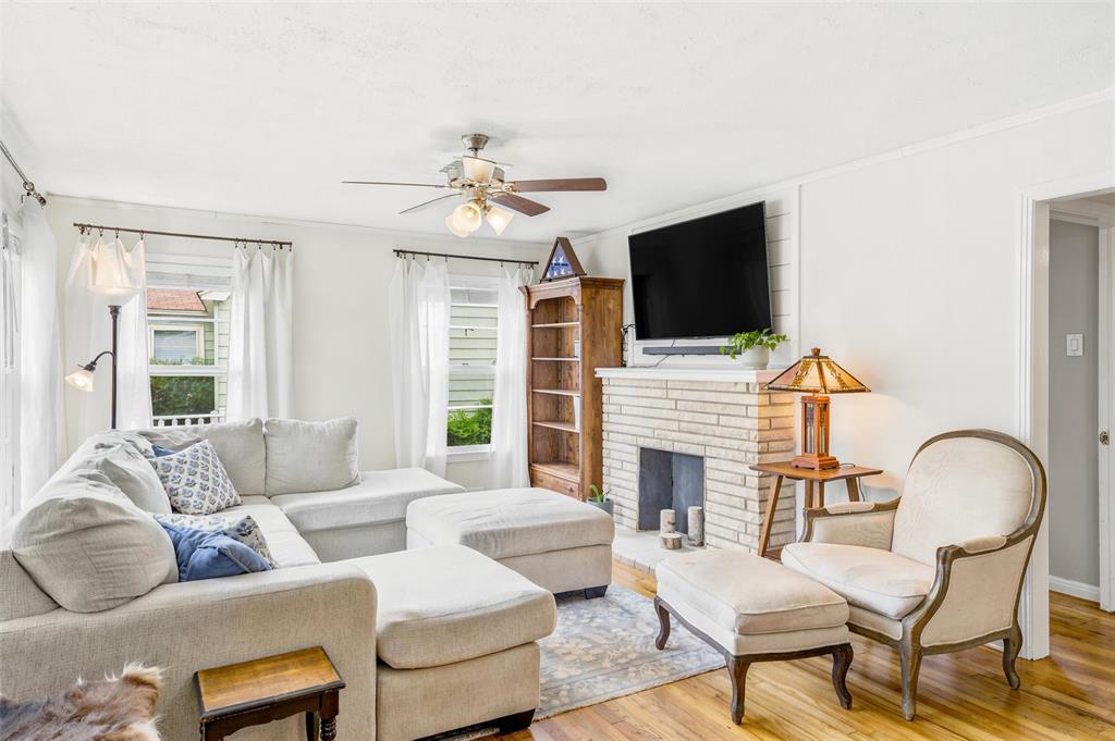 3012 Mitchell Avenue Waco, TX 76708 - Photo 2 of 18 Living area featuring wood-finish flooring, a white brick fireplace, multiple windows, and a ceiling fan with integrated lighting