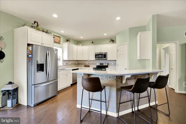 a kitchen with stainless steel appliances granite countertop a refrigerator a stove top oven and a center island with wooden floor