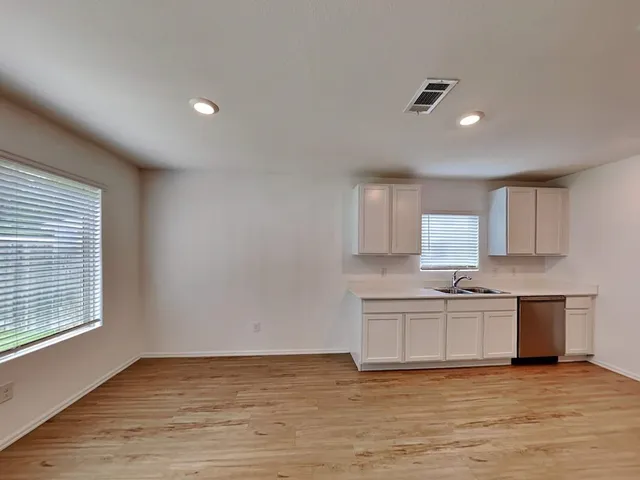a view of a kitchen with stainless steel appliances granite countertop a stove a sink white cabinets and a wooden floor