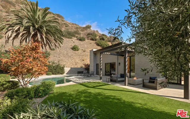 a view of a patio with table and chairs under an umbrella with large trees