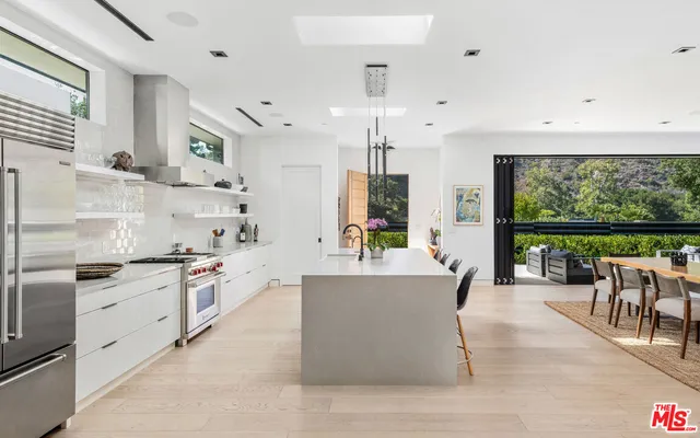 a large kitchen with stainless steel appliances a stove a sink dishwasher a oven with white cabinets and wooden floor