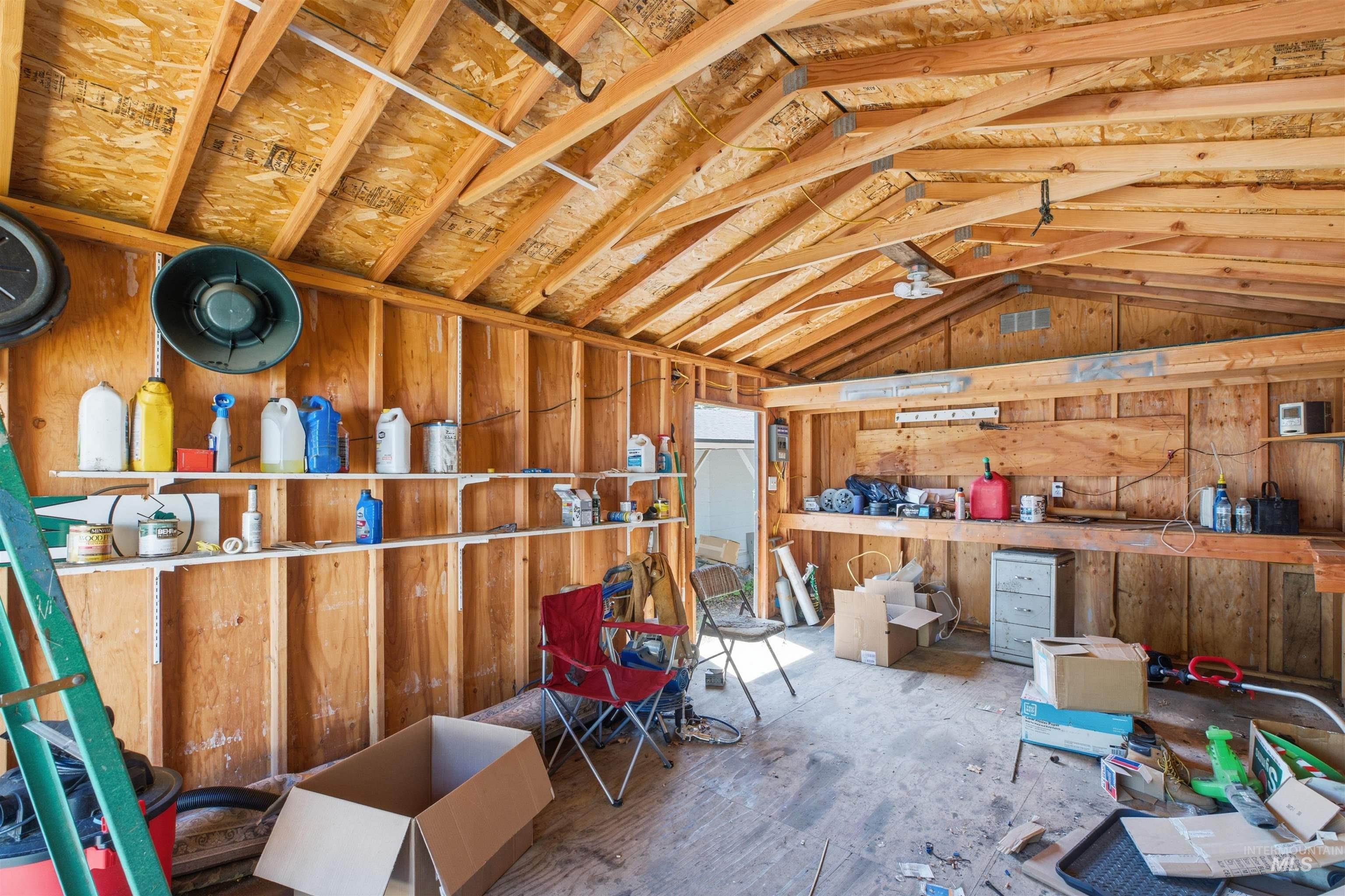 735 Oak Street Potlatch, ID 83855 - Photo 17 of 30 Exposed wood framing and ceiling trusses define this interior space, featuring a built-in workbench, wall-mounted shelving, and an overhead light fixture