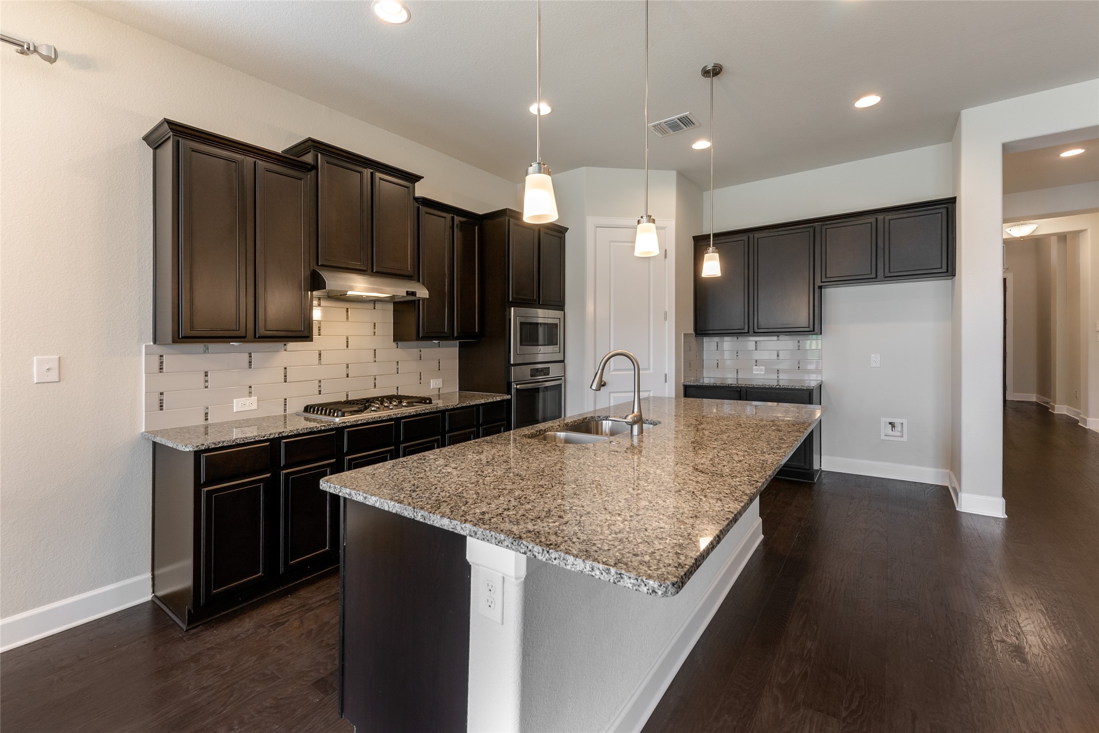3043 Hidalgo Loop Round Rock, TX 78665 - Photo 3 of 34 Kitchen featuring tasteful backsplash, light stone countertops, dark wood-style floors, and a kitchen island with sink