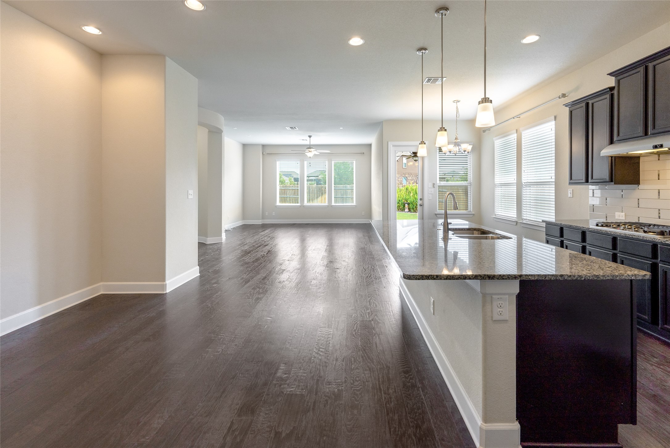3043 Hidalgo Loop Round Rock, TX 78665 - Photo 9 of 34 Kitchen featuring light stone counters, dark wood-style floors, a kitchen island with sink, tasteful backsplash, and dark wood finish cabinets