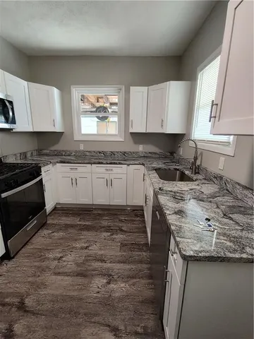 a kitchen with stainless steel appliances granite countertop a stove top oven a sink dishwasher and a microwave oven with white cabinets