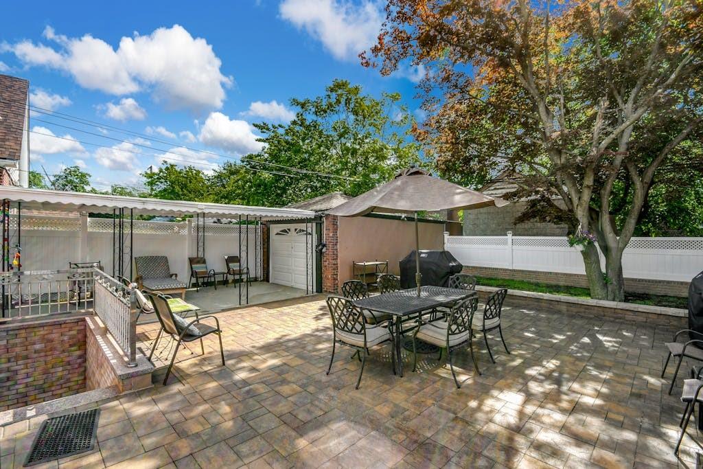 130-13 230th Street Queens, NY 11413 - Photo 11 of 12 a view of a patio with table and chairs under an umbrella with large trees