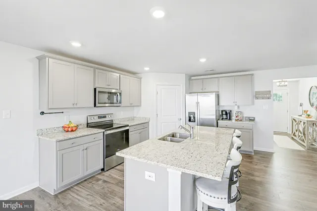 a kitchen with stainless steel appliances granite countertop a sink dishwasher a stove refrigerator and white cabinets with wooden floor