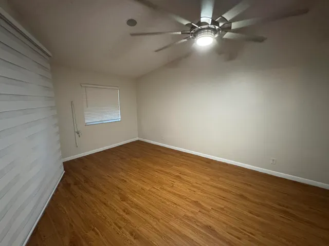 an empty room with wooden floor fan and windows