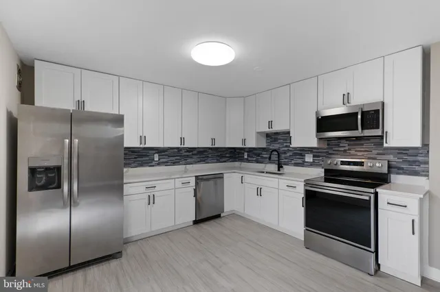 a kitchen with stainless steel appliances granite countertop a refrigerator a stove a sink and white cabinets