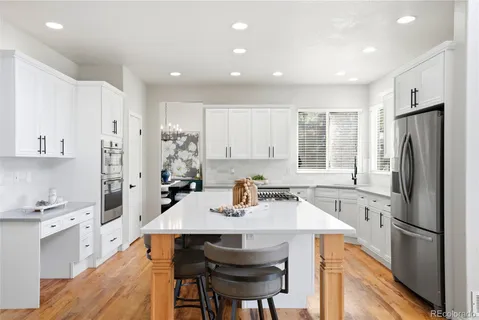 a kitchen with stainless steel appliances a sink a stove a refrigerator cabinets and a dining table with wooden floor