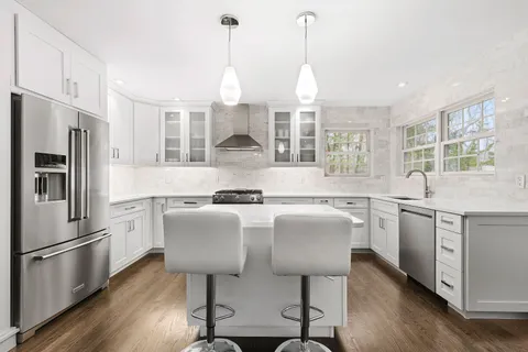 a kitchen with stainless steel appliances granite countertop a sink a stove a refrigerator cabinets wooden floor and a window