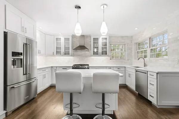 a kitchen with stainless steel appliances granite countertop a sink a stove a refrigerator cabinets wooden floor and a window