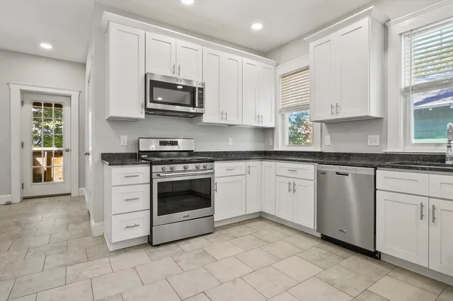 a white kitchen with granite countertop white cabinets and stainless steel appliances