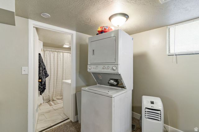 386 North 500 East Provo, UT 84606 - Photo 19 of 24 Laundry area featuring stacked washing machine and dryer, a textured ceiling, and light marble finish flooring