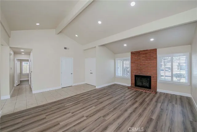 an empty room with wooden floor fireplace and windows