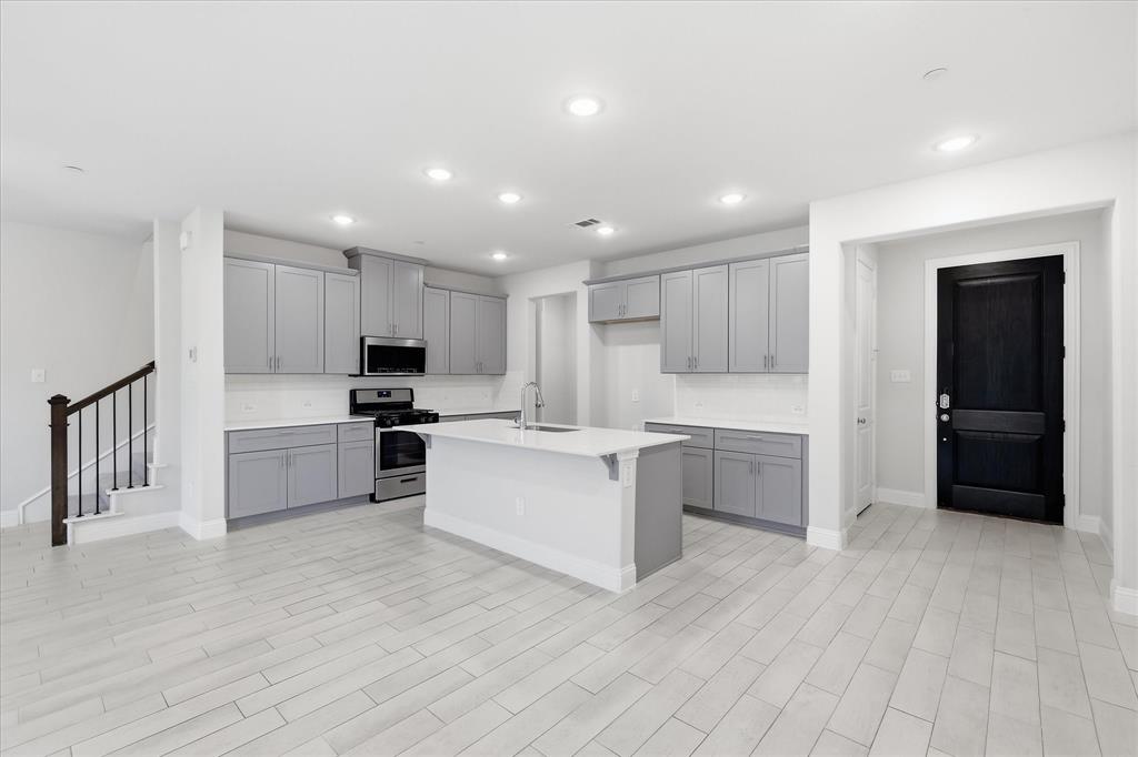519 Sequoia Street Allen, TX 75002 - Photo 11 of 38 Open-concept kitchen featuring an island with a sink, stainless steel appliances, shaker-style cabinetry, and light-toned flooring