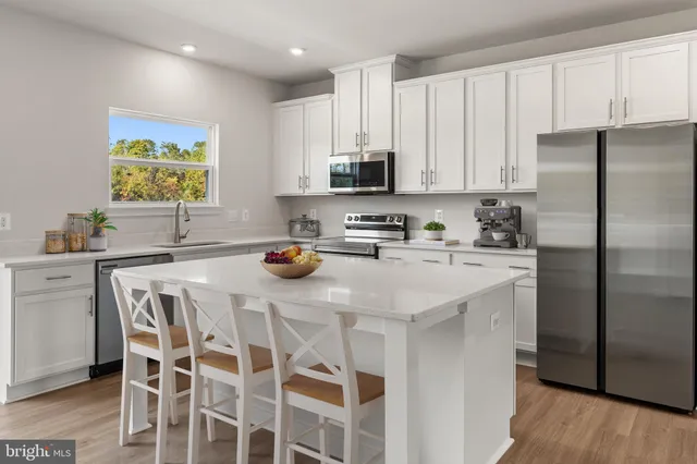 a kitchen with stainless steel appliances a white refrigerator a sink a stove a dining table and chairs with wooden floor