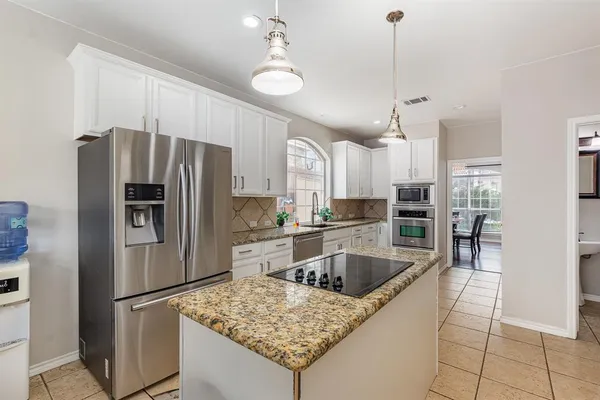 a kitchen with stainless steel appliances granite countertop a refrigerator a sink a stove a dining table and chairs