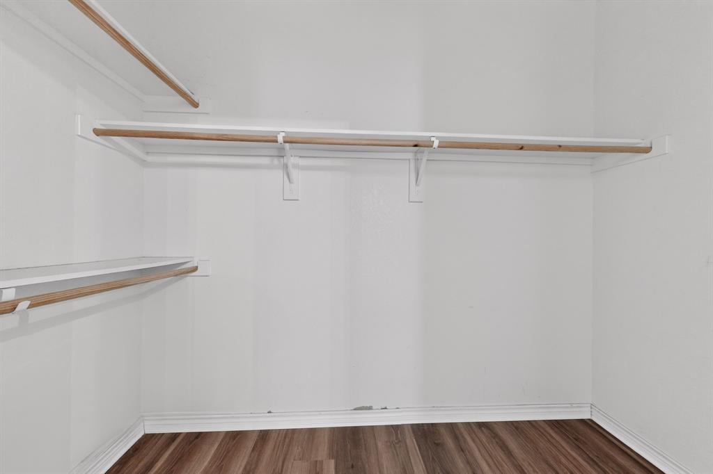 426 Harding Lane Lavon, TX 75166 - Photo 22 of 40 White closet interior featuring wood-finish flooring, white baseboards, and built-in white shelving with natural wood rods