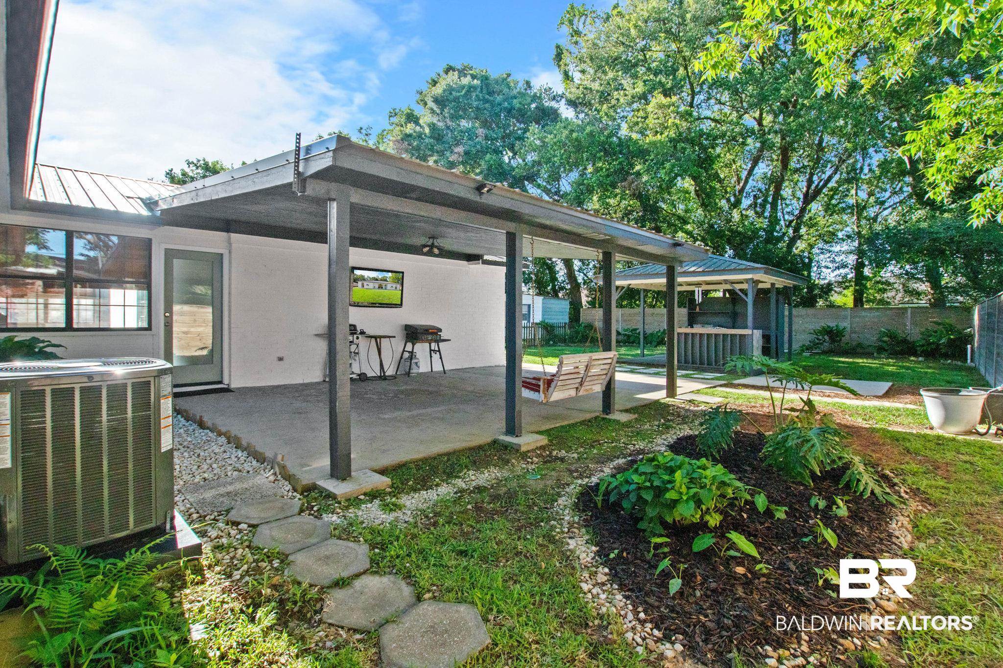 524 Ariel Avenue Foley, AL 36535 - Photo 25 of 37 Expansive backyard featuring a covered patio, a separate built-in grill station with a covered gazebo, mature trees, and landscaping beds with stone borders